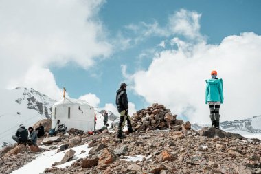 Kazbegi, Georgia - 18th september, 2024: Bethlehem Church and group of climbers stand on high viewpoint on acclimatization day. Climbing Mount kazbek preparation concept. clipart