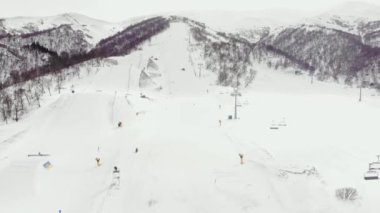 Karlı dağ yamaçları ve kış ağaçları olan kayak merkezinin hava manzarası. Bir grup insan Didveli tepesinden kayak yapmaya ve snowboard yapmaya gidiyor.