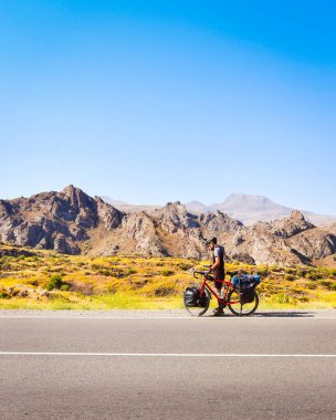 Bisikletçi yolda durdu. Bisiklet kontrol haritası açık havada kayboldu. Sıcak güneşli bir günde ıssız bir yerde. Sporcu bisikletçi, yol kenarındaki telefonu kontrol et. Dikey arkaplan