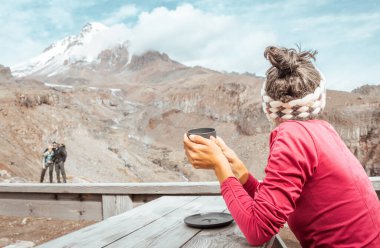 Kafkasyalı genç mutlu turist kadın dağda kafeteryada oturuyor sıcak çikolata içiyor Kazbek dağlarının zirvesini seyrediyor Kazbegi ulusal parkında. Gürcistan 'a sonbaharda seyahat