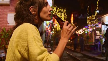 Heyecanlı beyaz kadın rayların kenarında durup içki içiyor ve Hanoi şehrindeki ünlü Hanoi tren sokağında geçen treni seyrediyor. Gece hayatı konsepti