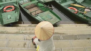 Ninh Binh, Vietnam - 15 Mart 2024: Turist kadın geleneksel Vietnam şapkası takıyor kürek çekerek doğanın tadını çıkarın. Hoa Lu Tam Coc, Hoi An Antik Kasabası. Ünlü Vietnam seyahati