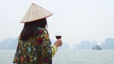Kadın turist, Vietnam 'daki Halong Körfezi milli parkında binlerce küçük ve büyük kireçtaşı adasından oluşan tekne turunun keyfini çıkarıyor. Vietnam 'a seyahat. Ellerinde kırmızı şarap olsun.