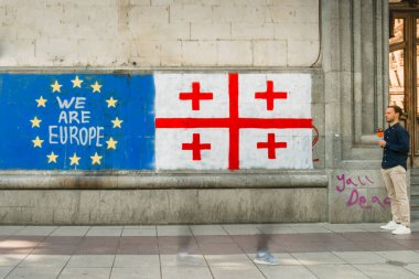 Tiflis, Gürcistan - 16 Mayıs 2024: Erkek muhabir sohbeti, başkent sokaklarında haber yaptı. Duvarda ünlü grafiti Eu ve Gürcistan bayrağı var. Rus hukuku hareketi yok. AB kavramına entegrasyon süreci