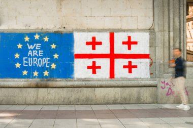 Erkek haber kanalı TV muhabiri Tiflis sokaklarında mikrofona konuştu. Duvarda ünlü grafiti Eu ve Gürcistan bayrağı var. Rus hukuku hareketi yok. AB kavramına bütünleşme süreci