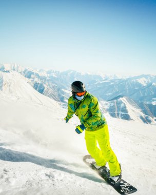 Ekstrem snowboardcu pudra sürüyor, elle sürüklüyor, güneşli dağ taşrasında güneşin üzerine kar püskürtüyor. Snowboardcu pistte kar kayağı yaparken eğleniyor.