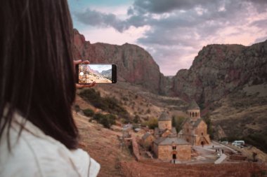 Yakın plan kadın Ermenistan 'daki Noravank Ortodoks Manastırı' nın fotoğrafını çekiyor. Kafkas dağlarındaki kırmızı renkli uçurumlarla çarpıcı bir gün batımı manzarası