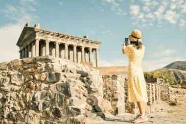 Yaz tatilinde Ermenistan 'da Garni Roma Tapınağı' nın fotoğrafını çeken genç turist kadın. Seyahat, tatil ve Avrupa 'nın simgeleri konsepti. Blogcu dünyayı dolaşır, simgeleri yakalar. Ermenistan Unesco siteleri