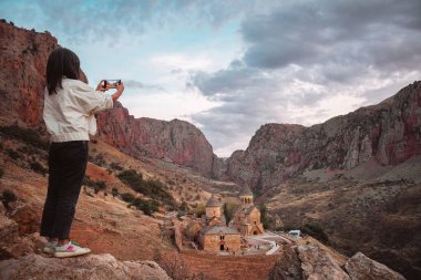 Yakın plan kadın Ermenistan 'daki Noravank Ortodoks Manastırı' nın fotoğrafını çekiyor. Kafkas dağlarındaki kırmızı renkli uçurumlarla çarpıcı bir gün batımı manzarası