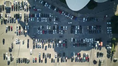 Zaman atlamalı hava zoom 'u, sabahleyin ofis binasının yanındaki büyük bir otoparkı gösteriyor. Araçlar park edilmiş. Güneşli bir sabahta kalabalık otoparkta arabalar hareket ediyor. Yüksek kalite 4k