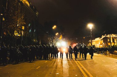 Tbilisi, Georgia - 1st december, 2024: special unit armored police sweeps streets at midnight from protestors in capital Tbilisi Rustaveli avenue. Georgia country protests and protestors for freedom clipart