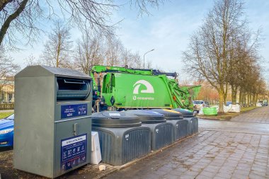 Siauliai, Litvanya - 15 Kasım 2024: Dar kentsel sokakta izole edilmiş yeşil çöp kamyonu Eco servis aracı ve soğuk bir günde iş yerinde çöp konteynırlarını yöneten şoför. AB geri dönüşümü
