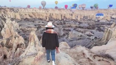 Panorama Kafkasyalı Kafkas Kadın blog yazarı yalnız gezgin ellerini kaldırarak Cappadocia 'daki uçuş sıcak hava balonlarına bakıyor. Aşk vadisi gün doğumu Kış sabahı