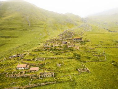 Tepenin yamacındaki terk edilmiş Arsha köyünün havadan görünüşü. Kazbegi Ulusal Parkı. Gürcistan Kafkasya dağlarında gizli mücevher manzarası
