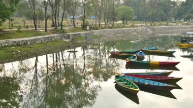 Zaman çizelgesi nepalli insanlar parkta yürürken rahatlayın ve günün tadını çıkarın. Tahta botlar Pokhara 'da gündoğumunda hafifçe sallanıyorlar. Phewa gölü tekne gezisi konsepti. Phewa rıhtımında çok renkli ahşap kayıklar ve katamaranlar.