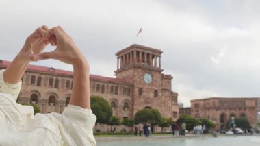 Fıskiyenin yanında duran genç bayan turist, Erivan, Ermenistan 'ın başkentindeki ünlü cumhuriyet meydanında elleriyle kalp şekli oluşturuyor. Gezgin Kafkasya 'da harika bir tatil geçiriyor.