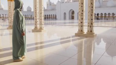 Abu Dabi, BAE - 25 Nisan 2025: Güzel günbatımında Abu Dabi 'deki Şeyh Zayed Büyük Camii' ni gezen kadın gezgin şık bir abaya giysisi giyiyor. Ücretsiz giriş camisi girişi ünlü hedef