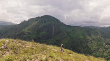 Kafkasyalı kadın turist Ella, Sri Lanka 'daki Little Adams Tepesi' nin zirvesine doğru manzaralı tepe boyunca yürüyüş yapıyor. Ella Kayası yemyeşil çay tarlalarının ve derin vadilerin üzerinde yükseliyor. Popüler Yürüyüş yolu