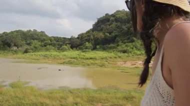 4x4 açık çatı aracında orman safarisindeki kadın, Sri Lanka, Dambulla yakınlarında sudaki vahşi bufaloları, yemyeşil ve tropikal vahşi yaşam alanlarıyla çevrili ulusal parklarla izliyor.