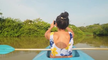 Arkadaki kadın çift mavi kano üzerinde oturup hayvan fotoğrafları çekiyor. Sri Lanka 'nın güneyindeki Tangalle Gölü' nün sakin sularında birkaç kano, yemyeşil mangrovlar ve tropikal doğayla çevrili.