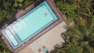 Hava manzaralı tropikal manzara. Genç kadın kristal berrak havuzda huzur içinde yüzüyor. Etrafı yemyeşil orman bitkileri ve palmiye ağaçlarıyla çevrili. İyilik ve refah tropikal adalarda geri çekiliyor.