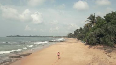 Gökyüzünden uzaklaşan kadın turist Tangalle kumsalında ve kayalık sahilde, Hint okyanusu sularında ve Sri Lanka 'nın güney kıyısında sallanan palmiyelerde yürüyor.