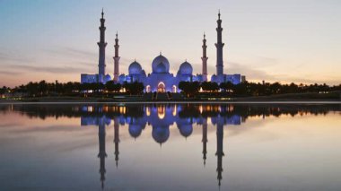 Günbatımında Şeyh Zayed Ulu Camii 'ni aydınlatan zaman dilimi, Abu Dabi, BAE. Turistler, Birleşik Arap Emirlikleri 'nde ünlü büyük camiyi geziyor. 4K yüksek kalite. Günbegün renkli.