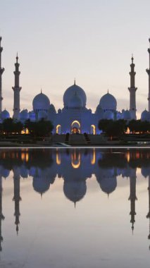 Günbatımında Şeyh Zayed Ulu Camii 'ni aydınlatan zaman dilimi, Abu Dabi, BAE. Turistler, Birleşik Arap Emirlikleri 'nde ünlü büyük camiyi geziyor. 4K yüksek kalite. Günbegün renkli.