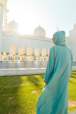 Abu Dabi, BAE - 25 Nisan 2025: Güzel günbatımında Abu Dabi 'deki Şeyh Zayed Büyük Camii' ni gezen kadın gezgin şık bir abaya giysisi giyiyor. Ücretsiz giriş camisi girişi ünlü hedef