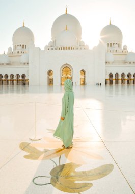 Abu Dabi, BAE - 25 Nisan 2025: Güzel günbatımında Abu Dabi 'deki Şeyh Zayed Büyük Camii' ni gezen kadın gezgin şık bir abaya giysisi giyiyor. Ücretsiz giriş camisi girişi ünlü hedef