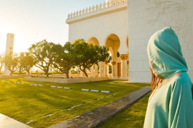 Abaya 'da kadın gezgin geleneksel kıyafetlerle BAE' deki büyük cami tapınağını ziyaret ediyor. Sütunların arasında yürüyen ve manzaraya bakan güzel beyaz kadın.
