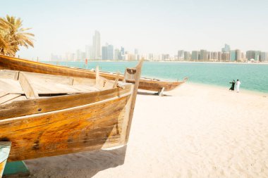 Abu Dabi silueti ve Birleşik Arap Emirlikleri 'ndeki Abu Dabi' deki Heritage Village 'da eski balıkçı tekneleri. Çift plajın keyfini çıkarıyor ve BAE 'deki turistik yerleri ziyaret ediyor.