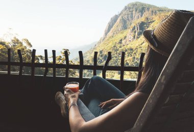 Sandalyede oturan kadın, Sri Lanka 'da nefes kesici Ella Rock manzarasıyla balkonda taze mango suyu içiyor. Srilanka 'da popüler turizm turizm merkezi. Blogger gezgini görünümleri sever