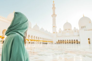 Abu Dabi, BAE - 25 Nisan 2025: Güzel günbatımında Abu Dabi 'deki Şeyh Zayed Büyük Camii' ni gezen kadın gezgin şık bir abaya giysisi giyiyor. İslam ve Modern Mimarinin Füzyonu