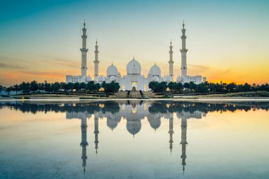 Şeyh Zayed Büyük Camii 'ni gün batımında, Abu Dabi, BAE' deki yansımalarıyla aydınlatmış. Turistler, Birleşik Arap Emirlikleri 'nde ünlü büyük camiyi geziyor. 4K yüksek kalite. Günbegün renkli.