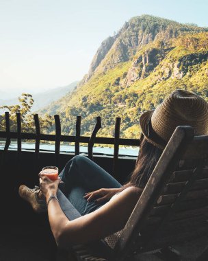 Sandalyede oturan kadın, Sri Lanka 'da nefes kesici Ella Rock manzarasıyla balkonda taze mango suyu içiyor. Srilanka 'da popüler turizm turizm merkezi. Blogger gezgini görünümleri sever