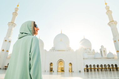 Abu Dabi, BAE - 25 Nisan 2025: Güzel günbatımında Abu Dabi 'deki Şeyh Zayed Büyük Camii' ni gezen kadın gezgin şık bir abaya giysisi giyiyor. Ücretsiz giriş camisi girişi ünlü hedef