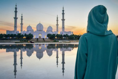 Geleneksel Arap elbiseli Abaya in Wahat Al Karama ya da Şeyh Zayed 'in Abu Dabi' deki Büyük Camii yakınlarındaki Haysiyet Vahası 'nda kültürel zarafet ve gün batımında ikonik İslami mimari sergiliyor.