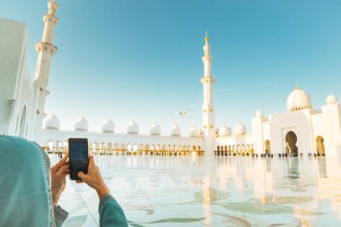 Turist, Abu Dabi 'deki Sheikh Zayed Büyük Camii' nin üzerine inen lüks özel jetin fotoğrafını çekiyor. Modern havacılık ve İslami mimari zenginlik, seyahat ve kültür simgelerini ön plana çıkarıyor