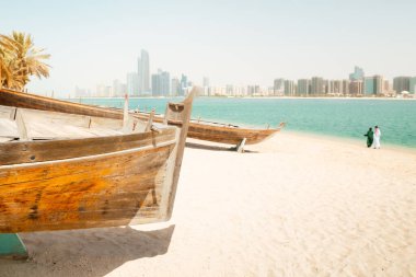 Abu Dabi silueti ve Birleşik Arap Emirlikleri 'ndeki Abu Dabi' deki Heritage Village 'da eski balıkçı tekneleri. Çift plajın keyfini çıkarıyor ve BAE 'deki turistik yerleri ziyaret ediyor.