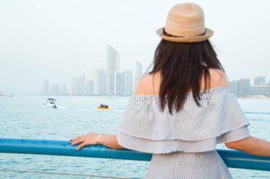 Abu Dhabis 'in göz kamaştırıcı arkaplanının karşısında kendine güvenen genç bir kadın, BAE' yi tanımlayan çeşitlilik ve ayrıcalık ruhunu somutlaştıran renkli bir türban takıyor.