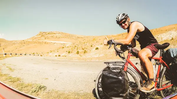Kafkasya dağlarında terkedilmiş otoyolun başparmakları üzerinde bisiklet kamerasına bakan sağlıklı ve sağlıklı beyaz erkek bisikletçi portresi. Dünyayı dolaşmak bisiklet turu sancak sancağını gezmek