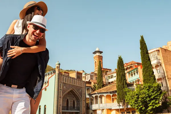 Tatilde Tiflis caddesinde yürüyen romantik çift turistleri - tatilde birlikte gülen mutlu arkadaşlar - insanlar ve tatil kavramı. Kadını taşıyan adam seyahatlerin tadını çıkarır.