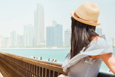 Kafkasyalı güzel turist kadının portresi Abu Dabi ufuk çizgisi manzarası ve plajına bakıyor. BAE 'deki barış, rahatlama ve kentsel güzelliği yansıtıyor.