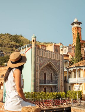 Yazlık hasır şapkalı bir kadın Tiflis, Georgia 'nın canlı mimarisine hayran kaldı. Geleneksel ahşap balkonlar, cami minaresi ve tarihi binalar. Seyahat, gezi, yaz tatili.
