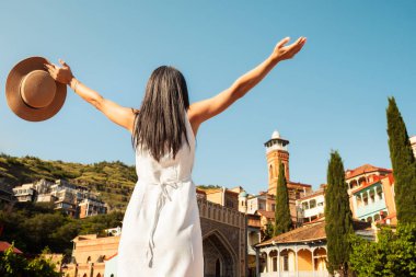 Beyaz elbiseli kadın kollarını kaldırarak cami kulesi ve geleneksel balkonları güneşli yaz günü olan renkli Tiflis eski kasaba mimarisinin keyfini çıkarıyor. Gürcistan 'da tarihi yerleri gezmek