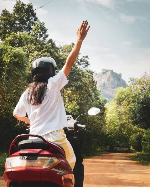 Kiralık scooter kullanan bir kadın güneşli bir günde güneşli bir günde güneşli bir günde Sri Lanka 'da Pidurangala ve Sigirya Kayası' nı ziyaret ediyor.