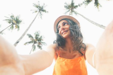 40 'lı yaşlardaki doğal beyaz kadın, tropikal adalarda palmiye ağaçları ve mavi gökyüzü ile çevrili tatilde kameraya selfie gülümsemesi sergiliyor. Zarif Yaşlanma konsepti. Güzelliği, bilgeliği, zaman içinde kendine güveni kucaklayan