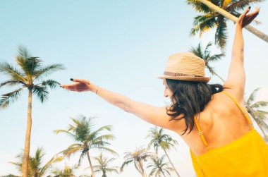 Genç kaygısız mutlu kadın gezgin sarı yazlık elbiseler giyer hasır şapka giyer tropik tatil yerlerinde Palm Beach 'in tadını çıkarır. Turizm turu kaygısız tatil atmosferi tropik seyahat tatili