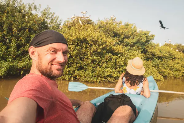 Kafkas turist çifti çift mavi kanoya oturup el sallıyor. Bereketli mangrovlar ve tropikal doğa ile çevrili sakin sularda birkaç kano.